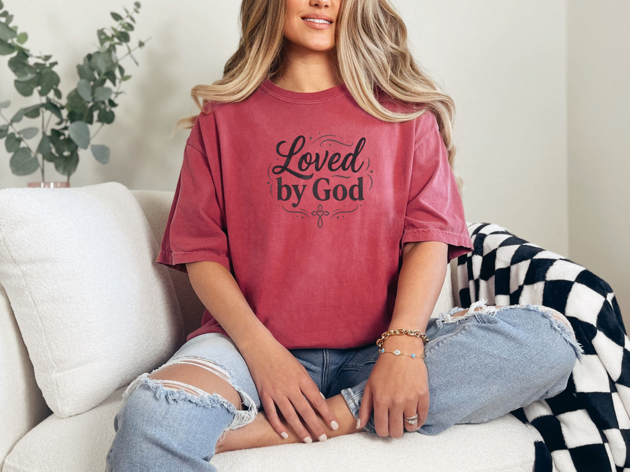 Woman sitting on a couch wearing a Loved by God T-Shirt, showcasing a comfortable and stylish design.