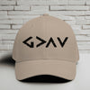 God is Greater Than Highs and Lows Embroidered Flexfit Hat displayed on a table against a brick background.
