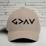 God is Greater Than Highs and Lows Embroidered Flexfit Hat displayed on a table against a brick background.