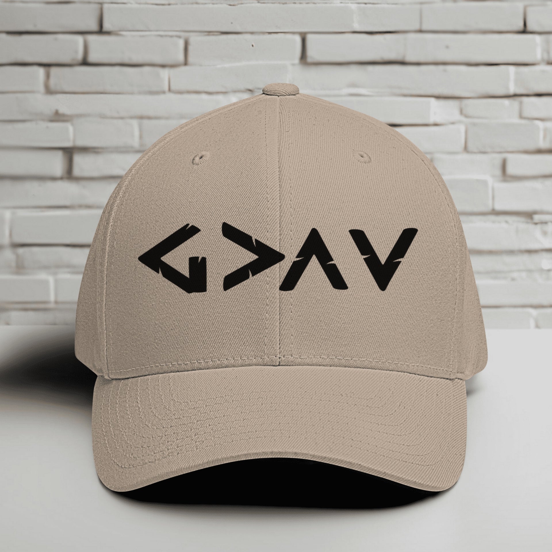 God is Greater Than Highs and Lows Embroidered Flexfit Hat displayed on a table against a brick background.