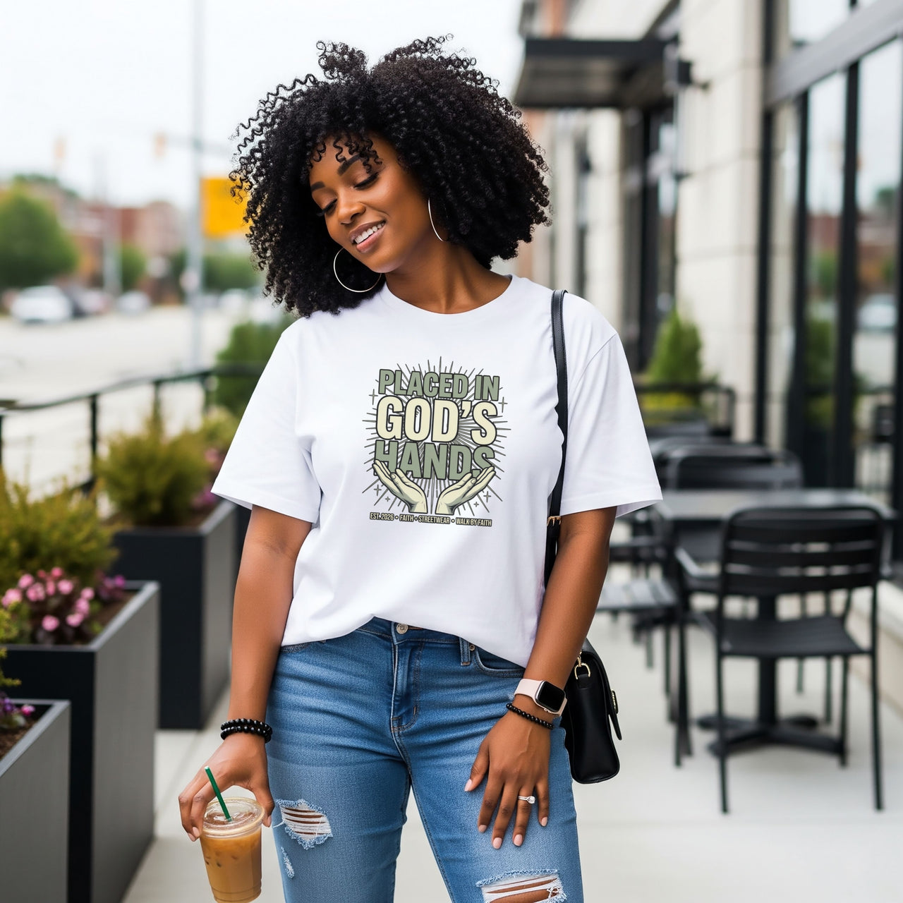 Model wearing a Placed in God's Hands T-Shirt, enjoying coffee outside in a casual urban setting.