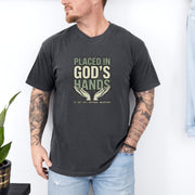 Placed in God's Hands T-Shirt worn by a man, featuring a design with hands and a comforting message of faith.