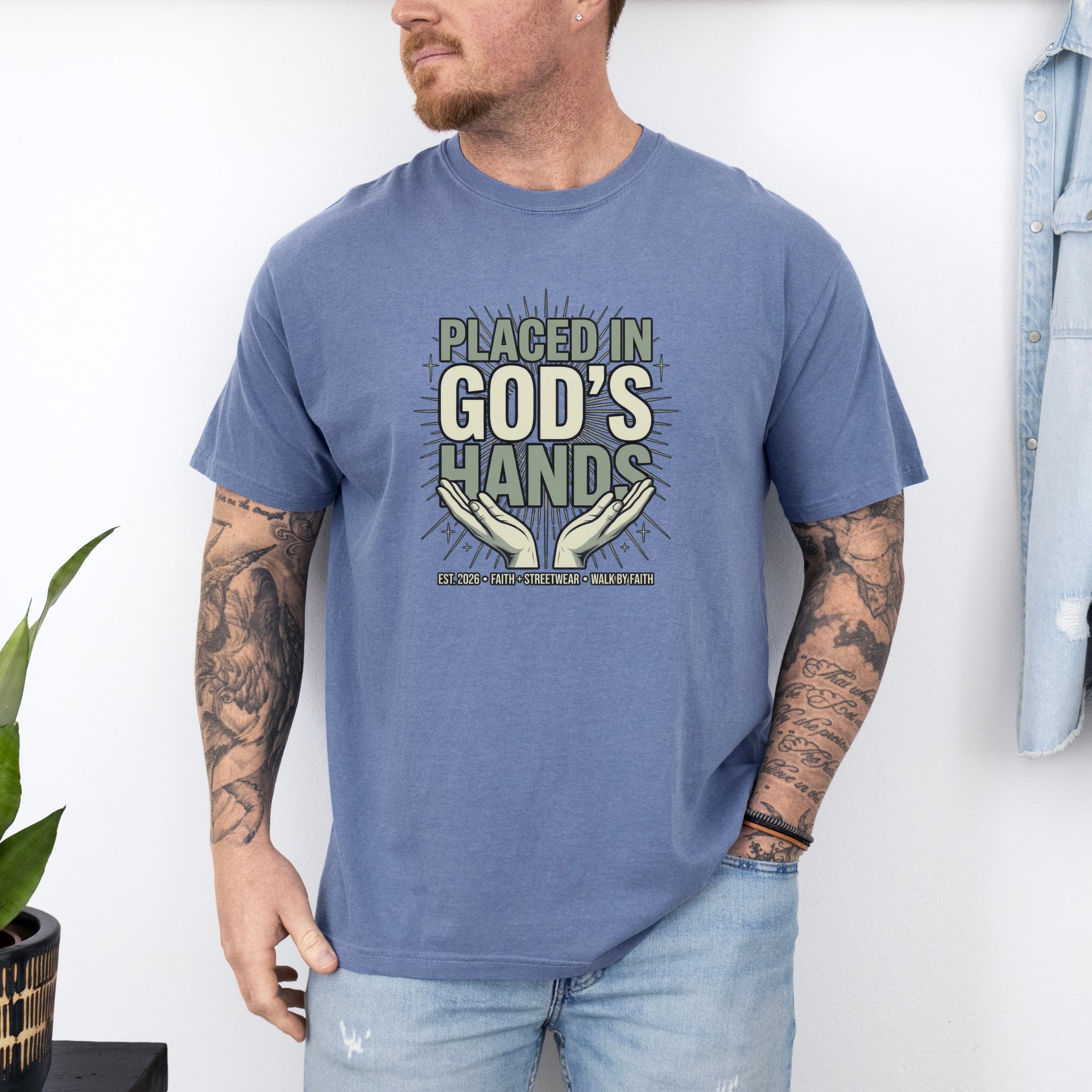Man wearing a blue Placed in God's Hands T-Shirt with a motivational design featuring hands and the phrase.