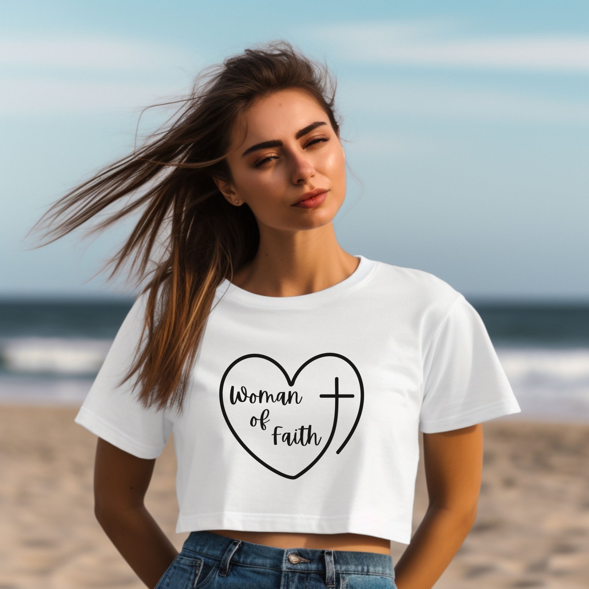 Woman Of Faith Heart Cross Crop Tee worn by a woman on the beach, featuring a heart and cross design.