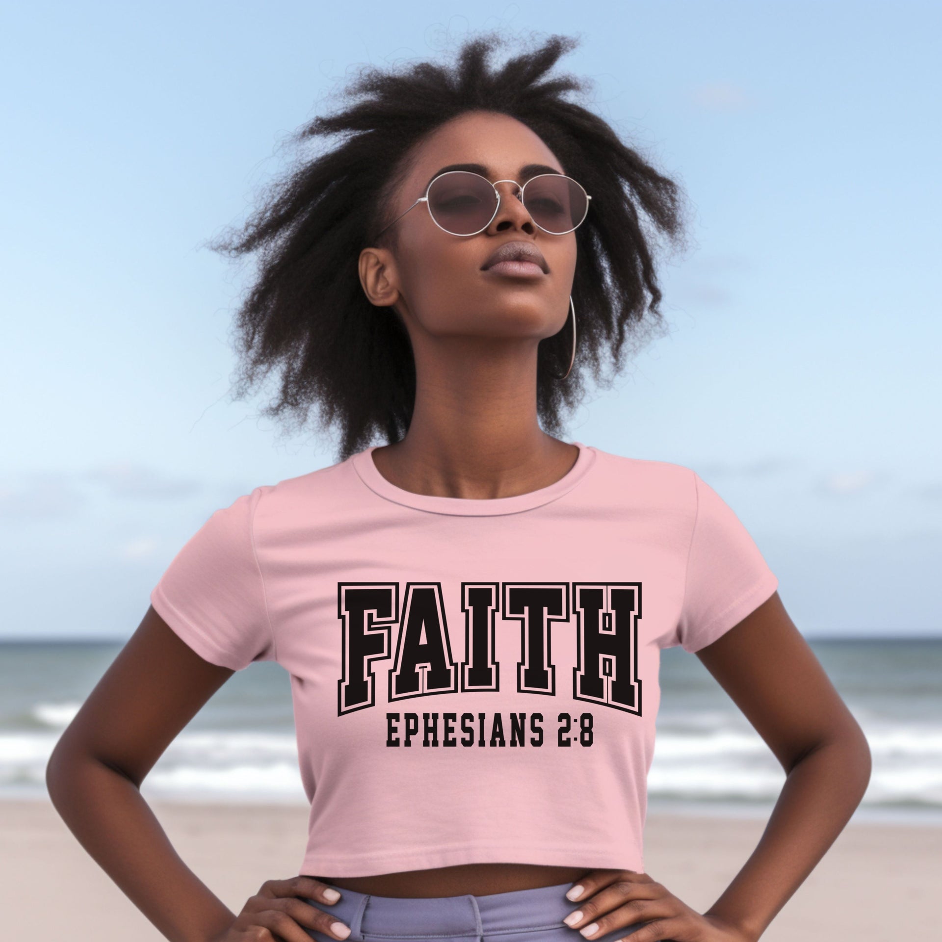 Faith Ephesians 2 8 Crop Tee worn by a model at the beach, showcasing its stylish design and inspirational message.