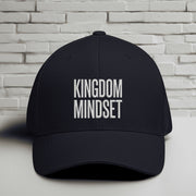 Kingdom Mindset Embroidered Flexfit Hat displayed against a simple brick wall background, emphasizing faith and intention.
