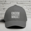 Kingdom Mindset Embroidered Flexfit Hat displayed on a table against a white brick background.