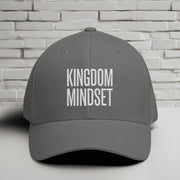 Kingdom Mindset Embroidered Flexfit Hat displayed on a table against a white brick background.