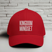 Kingdom Mindset Embroidered Flexfit Hat displayed on a table against a brick wall background.