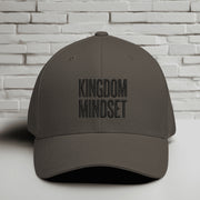 Kingdom Mindset Embroidered Flexfit Hat displayed against a brick wall background, emphasizing faith and style.