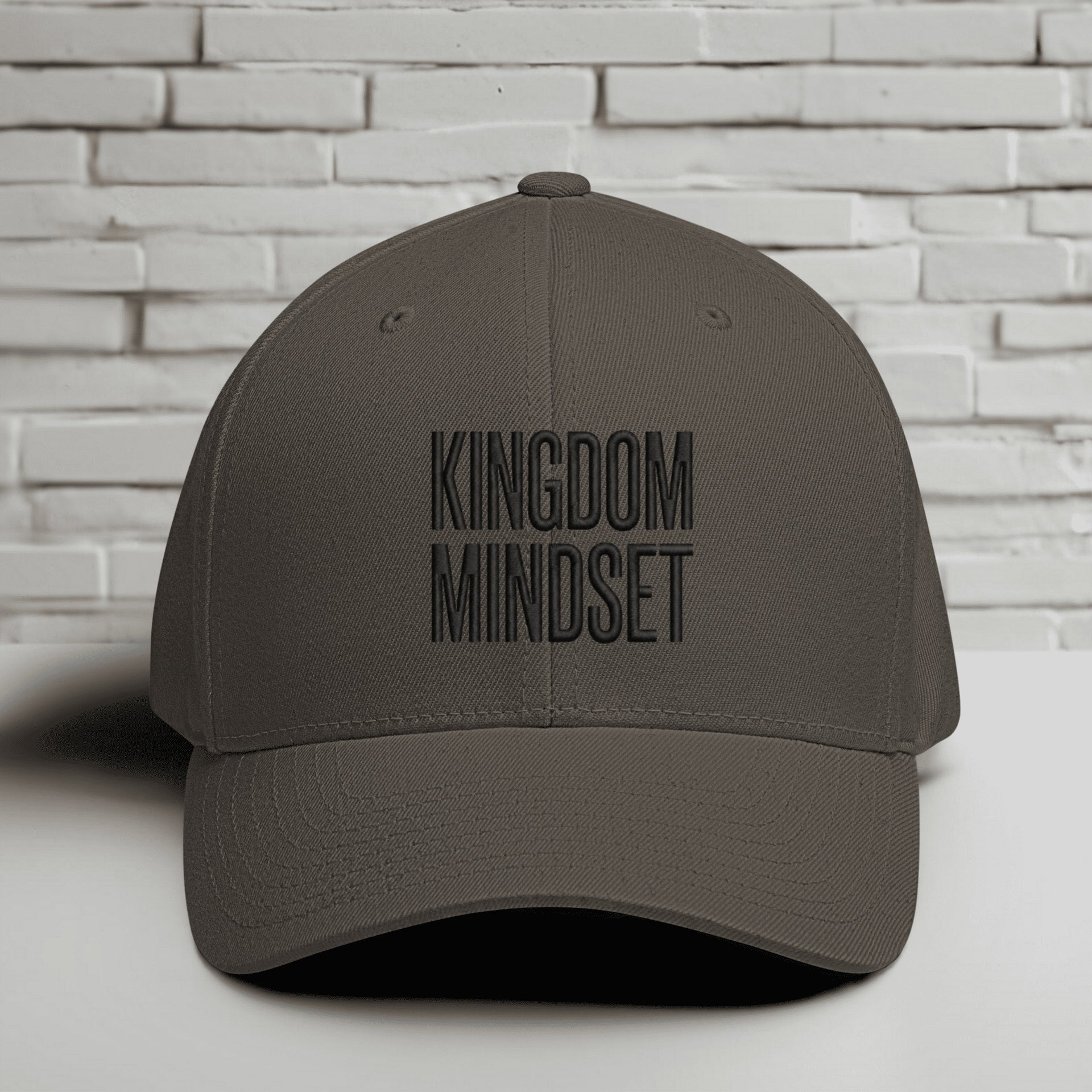 Kingdom Mindset Embroidered Flexfit Hat displayed against a brick wall background, emphasizing faith and style.