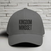 Kingdom Mindset Embroidered Flexfit Hat displayed against a textured white brick background.