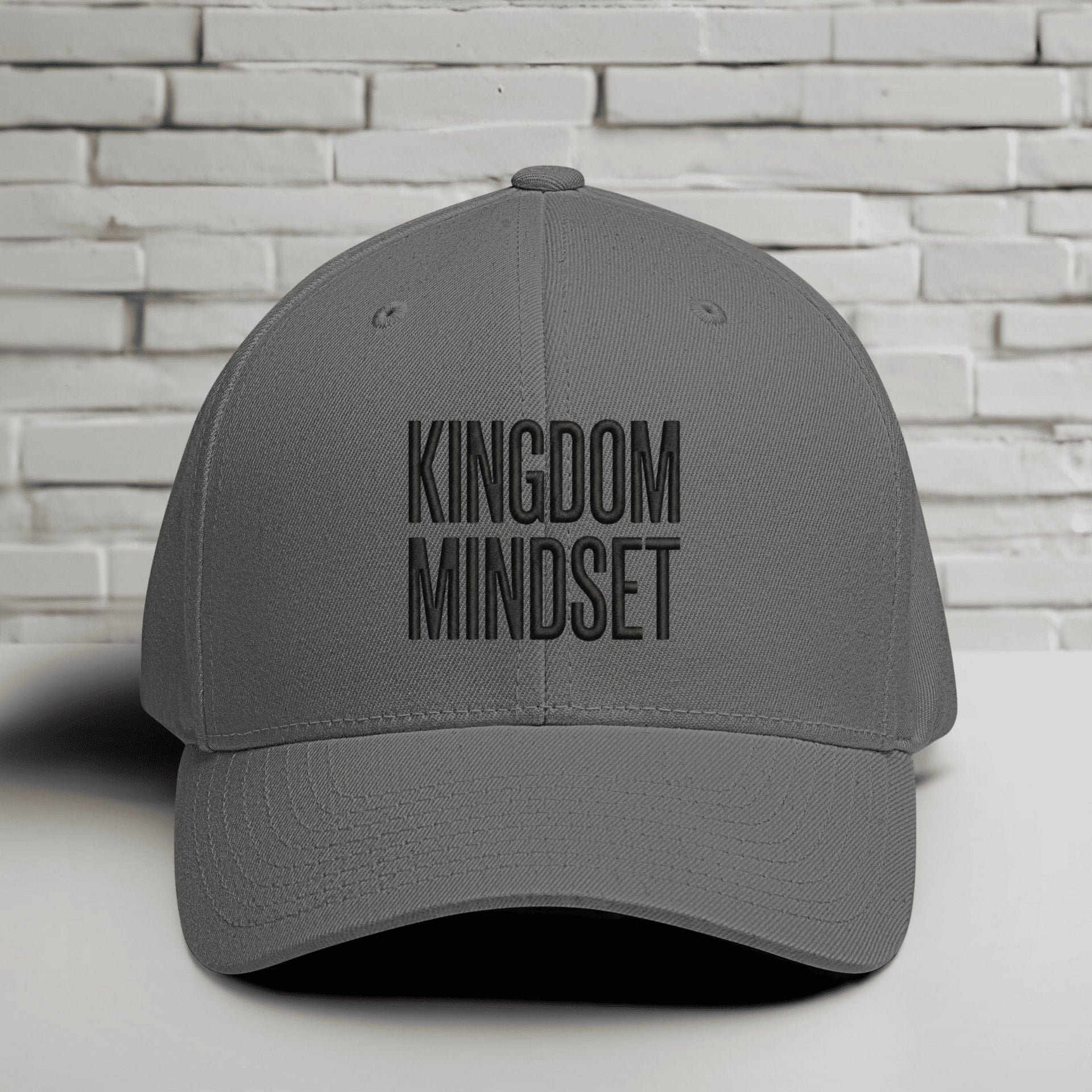 Kingdom Mindset Embroidered Flexfit Hat displayed against a textured white brick background.