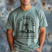 Faith Over Fear Trust In His Plan Comfort Colors T Shirt worn by a man with a cross design on a blue background.