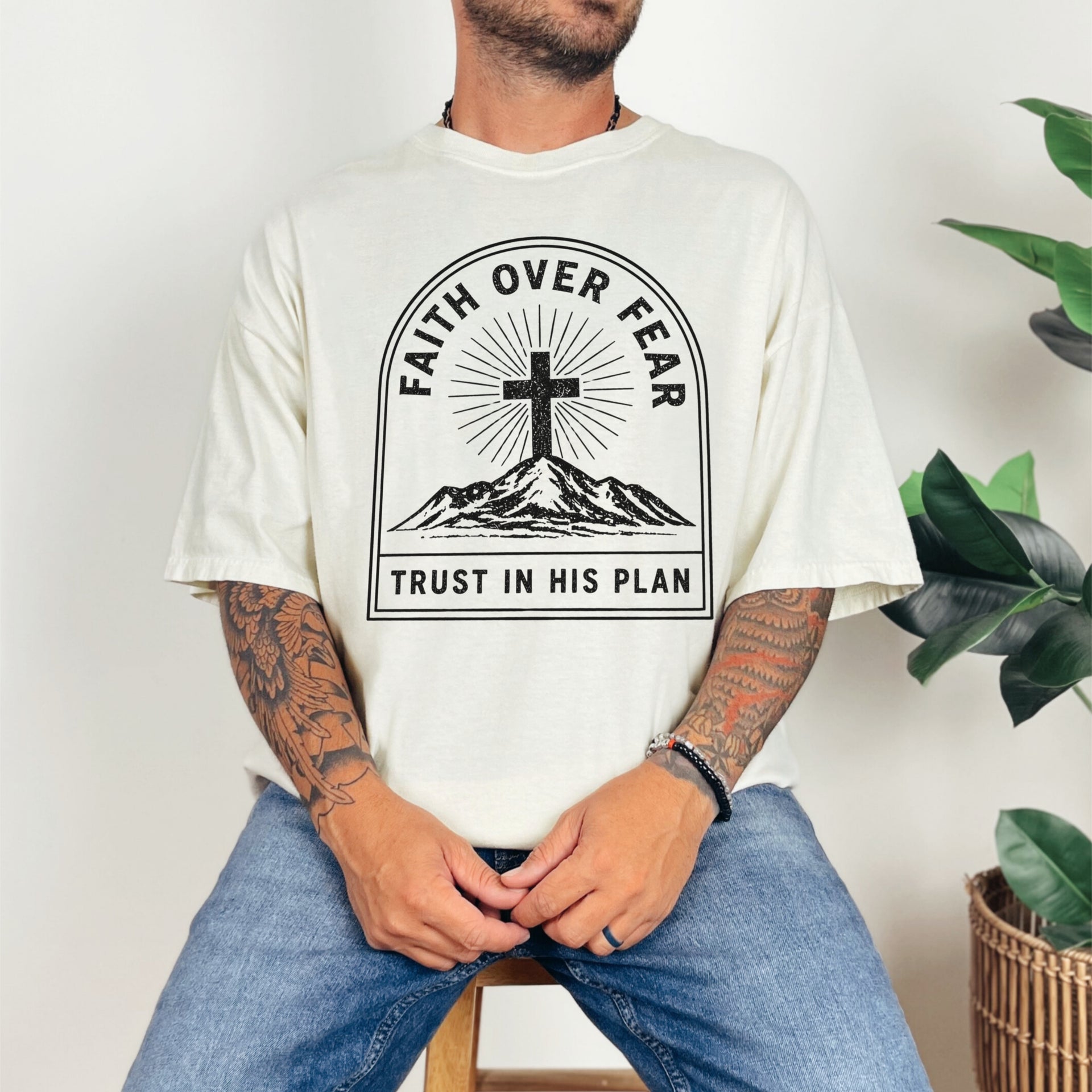 Faith Over Fear Trust In His Plan Comfort Colors T Shirt displayed by a model with tattoos and indoor plants.