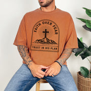 Faith Over Fear Trust In His Plan Comfort Colors T Shirt worn by a man, featuring a mountain and cross design.