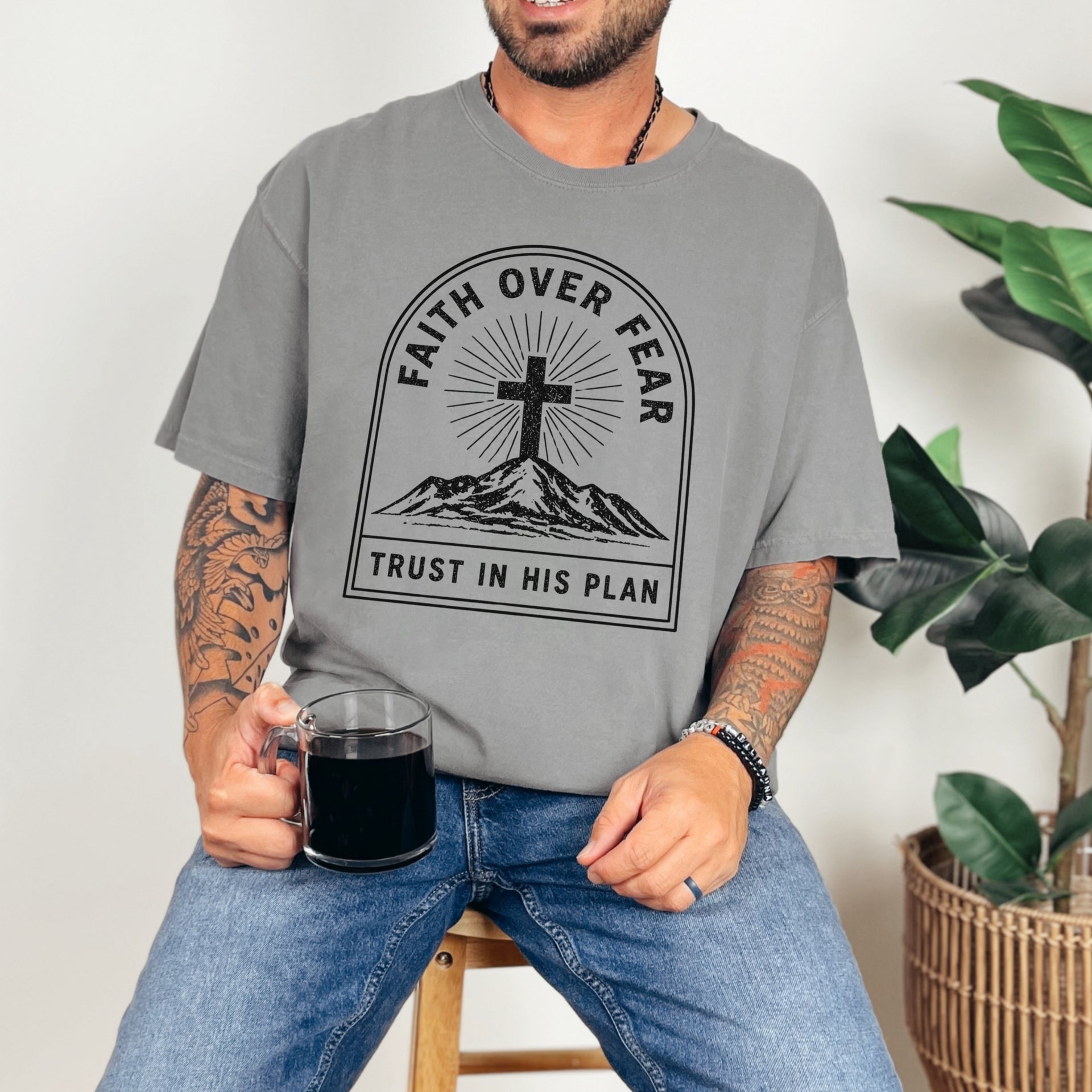 Faith Over Fear Trust In His Plan Comfort Colors T Shirt worn by male model holding a cup, featuring a cross and mountain design.