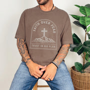 Faith Over Fear Trust In His Plan Comfort Colors T Shirt worn by a man with tattoos sitting near a plant.