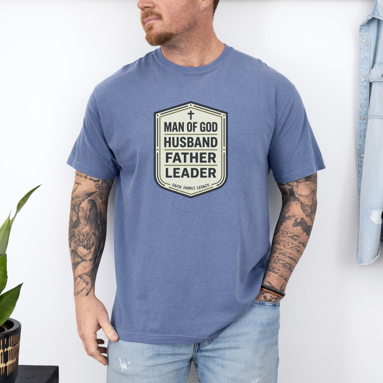 Man Of God Husband Father Leader T Shirt worn by a man with tattoos, showcasing a bold badge-style design.