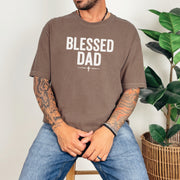 Man wearing a Blessed Dad Cross T Shirt with a bold design sitting near a plant, celebrating faith and fatherhood.