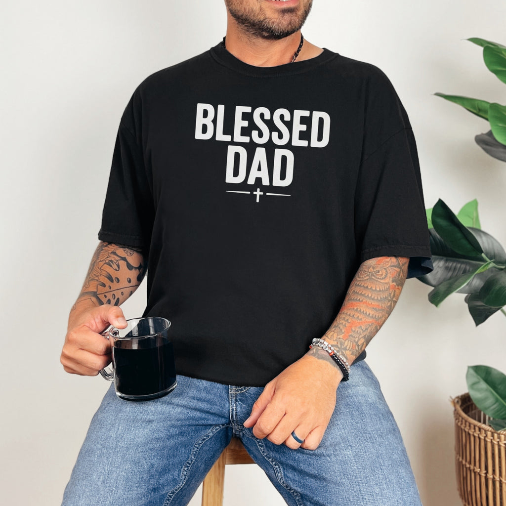 Man wearing a Blessed Dad Cross T Shirt, holding a mug, showcasing a bold design and relaxed style.