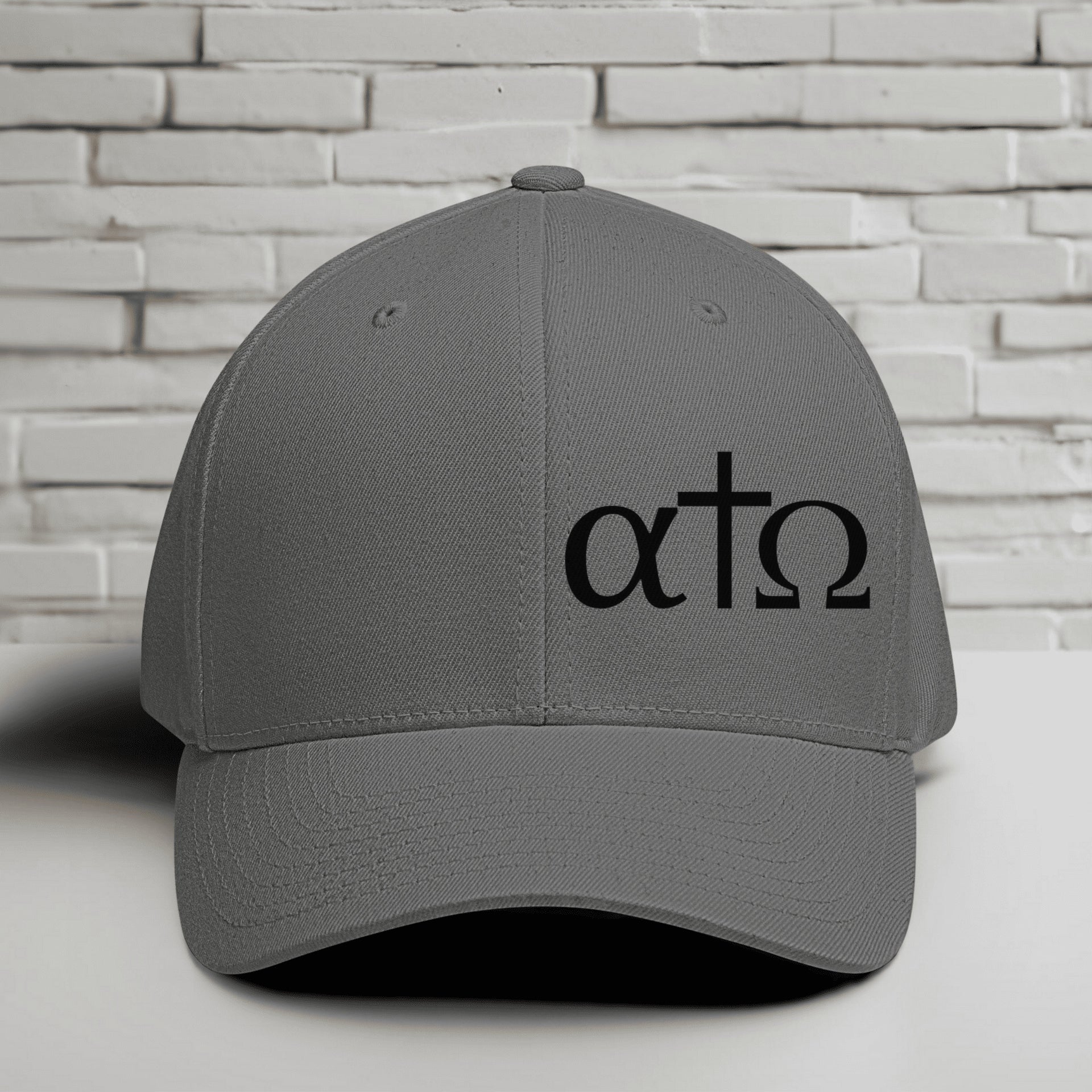 Alpha Omega Cross black hat with Greek letters on a gray Flexfit cap against a brick background.