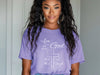 Model wearing a purple Love God T Shirt with scripture design, showcasing faith and style.