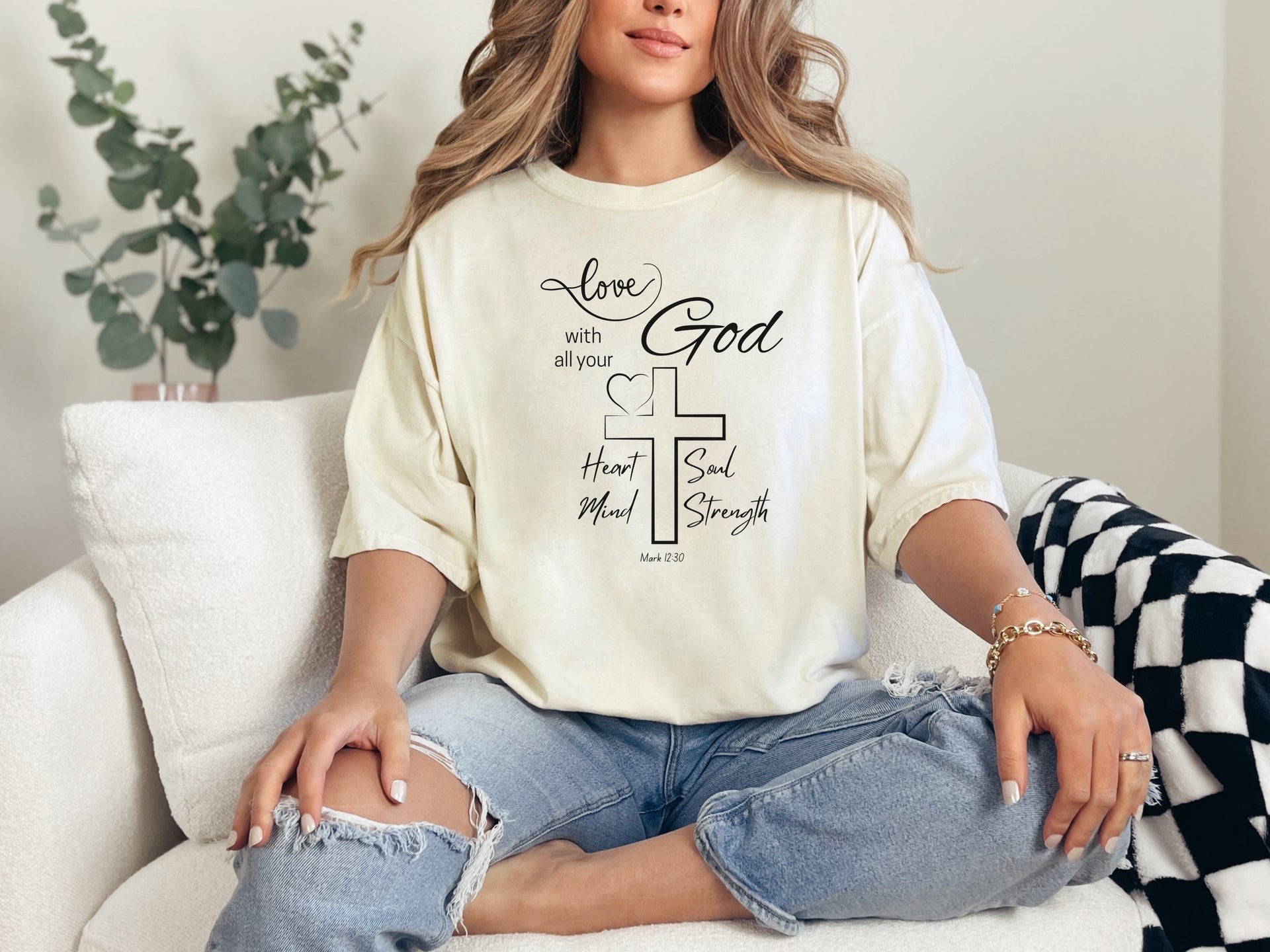 Woman wearing a Love God T Shirt with Mark 12:30 design, showcasing comfort and faith in a cozy setting.