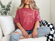 love God t shirt worn by a woman on a couch, featuring a cross design and scripture Mark 12:30.
