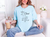 Woman wearing a light blue love God T shirt, relaxed at home, with coffee, showcasing faith-inspired design.