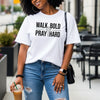Woman wearing Walk Bold Pray Hard Christian cross t shirt, showcasing faith and style in a casual urban setting.