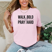 A woman wearing a pink Walk Bold Pray Hard Christian cross t shirt, showcasing a stylish design and relaxed fit.