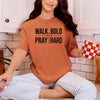 Woman wearing a Walk Bold Pray Hard Christian cross t shirt while sitting with a coffee mug in a kitchen.