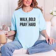 Woman wearing a blue Walk Bold Pray Hard Christian cross t shirt, sitting comfortably with a drink.