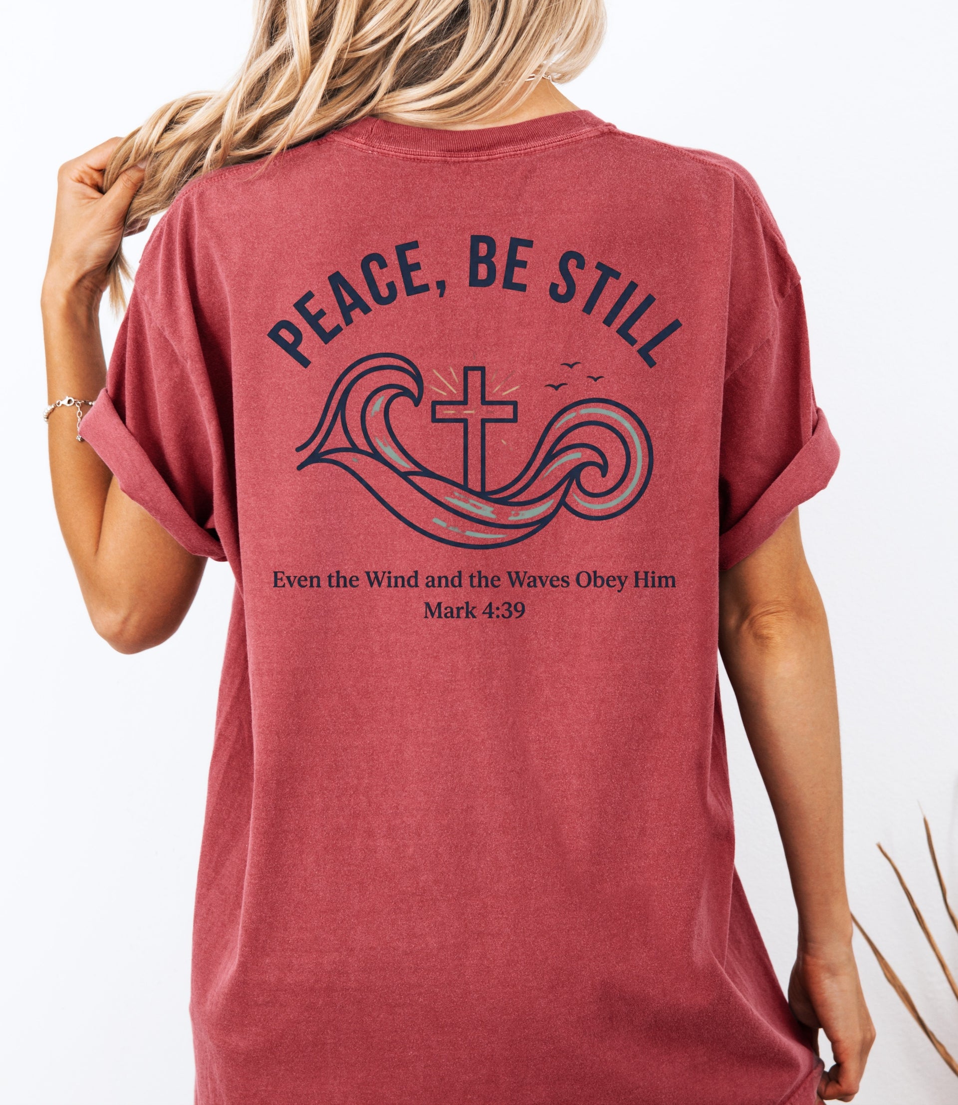 Model wearing a Peace Be Still T Shirt featuring waves and a cross design, symbolizing comfort in faith.