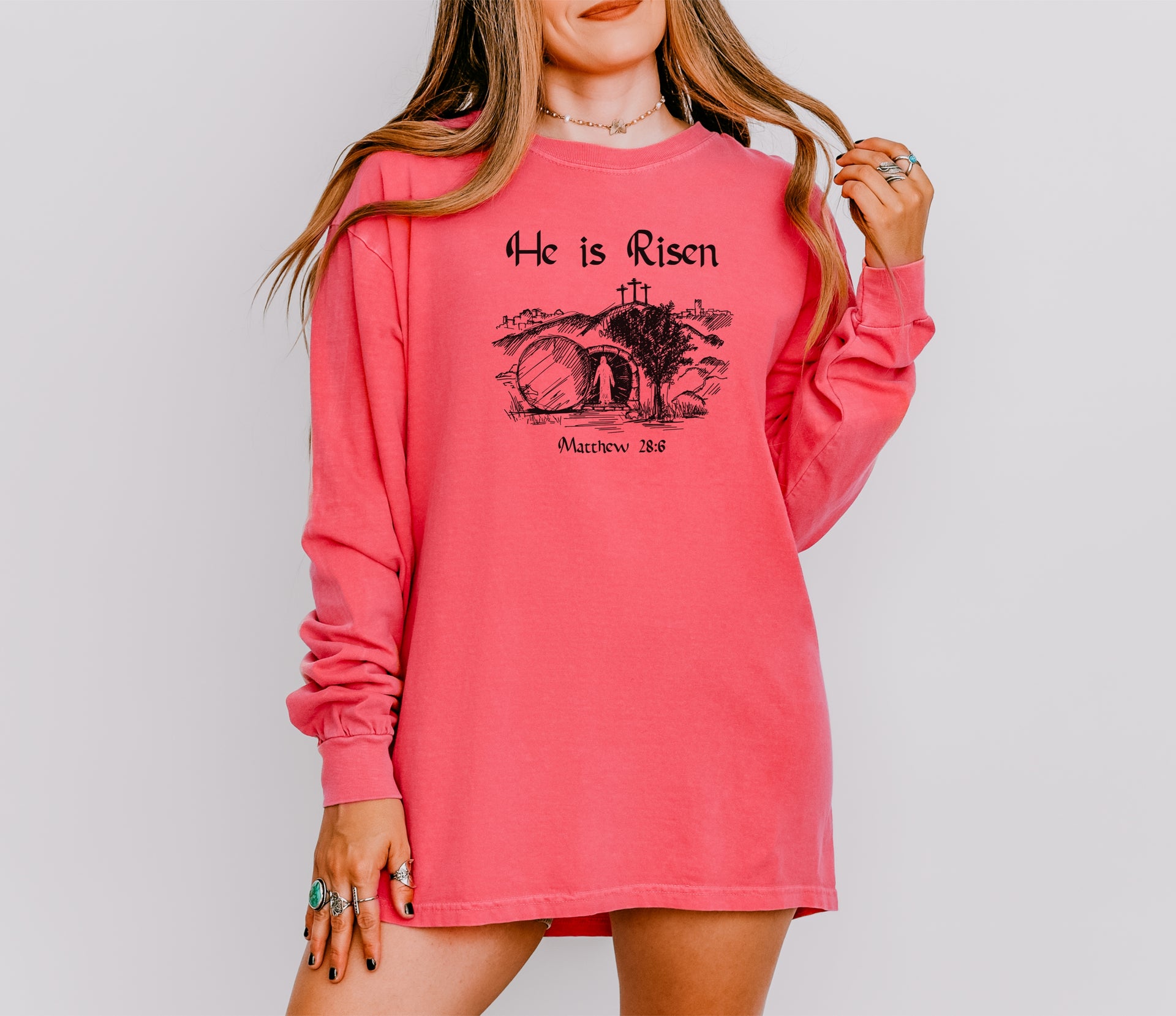 He Is Risen long sleeve t-shirt displayed on a model, featuring a graphic design with Matthew 28:6.