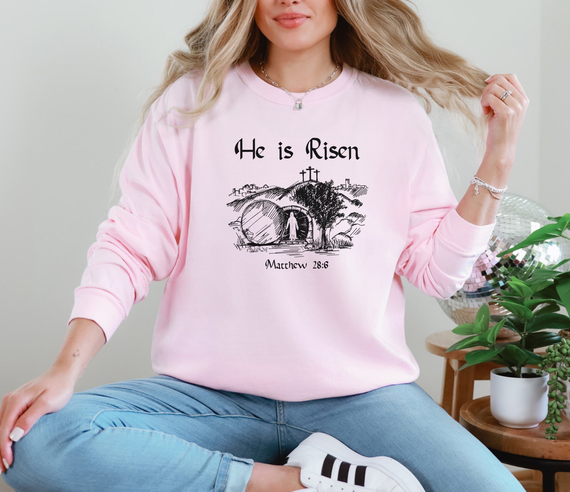 He Is Risen long sleeve t-shirt worn by a woman in a pink sweatshirt with a Christian resurrection design.