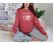 He Is Risen long sleeve t-shirt displayed on a woman sitting on a couch with a soft background.