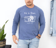 He Is Risen long sleeve t-shirt worn by a man, featuring a Christian design with Matthew 28:6, in a relaxed fit.