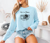 He Is Risen long sleeve t-shirt displayed on a woman in a living room setting.