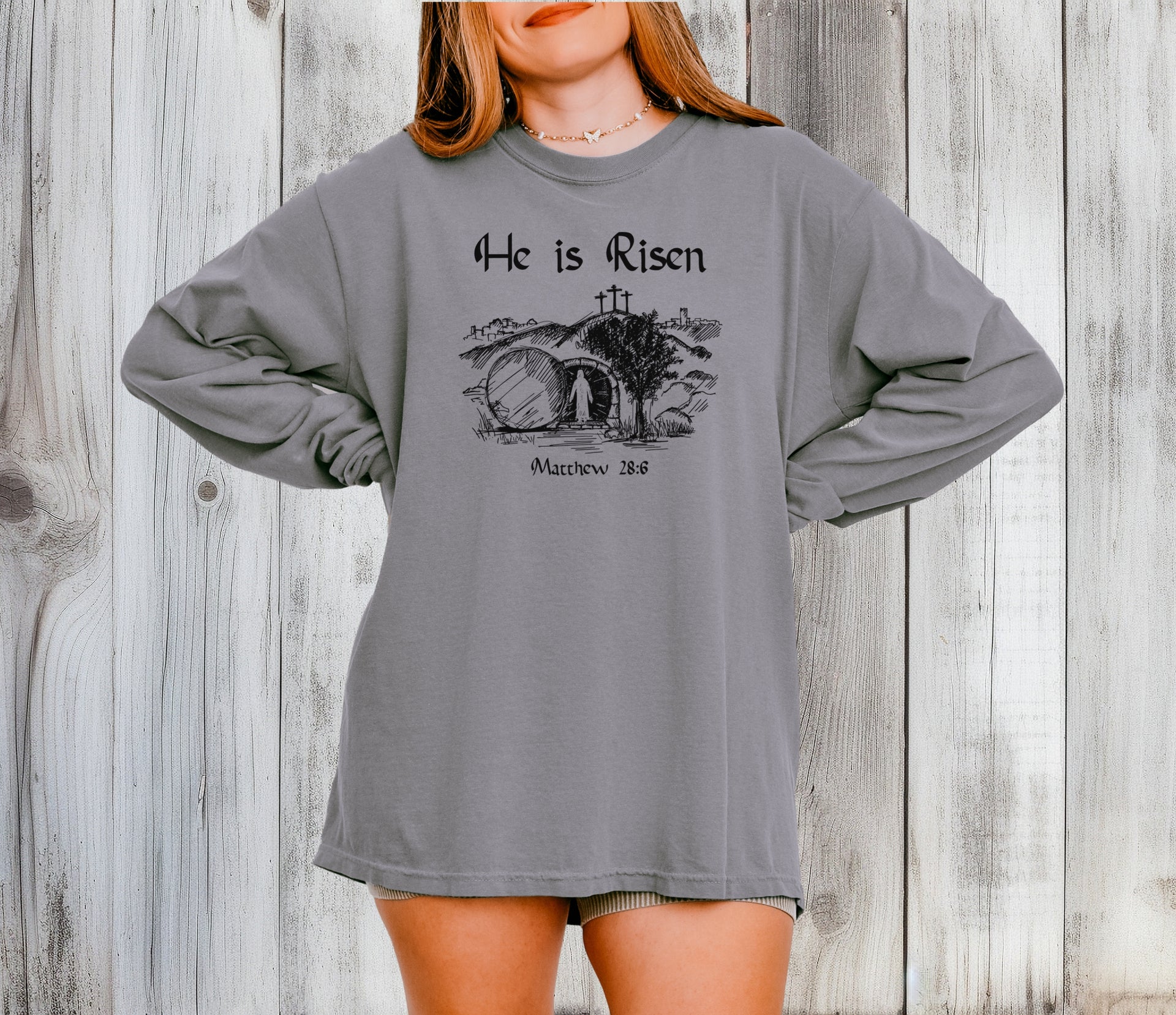 He Is Risen long sleeve t-shirt displayed on a model against a rustic wooden background.