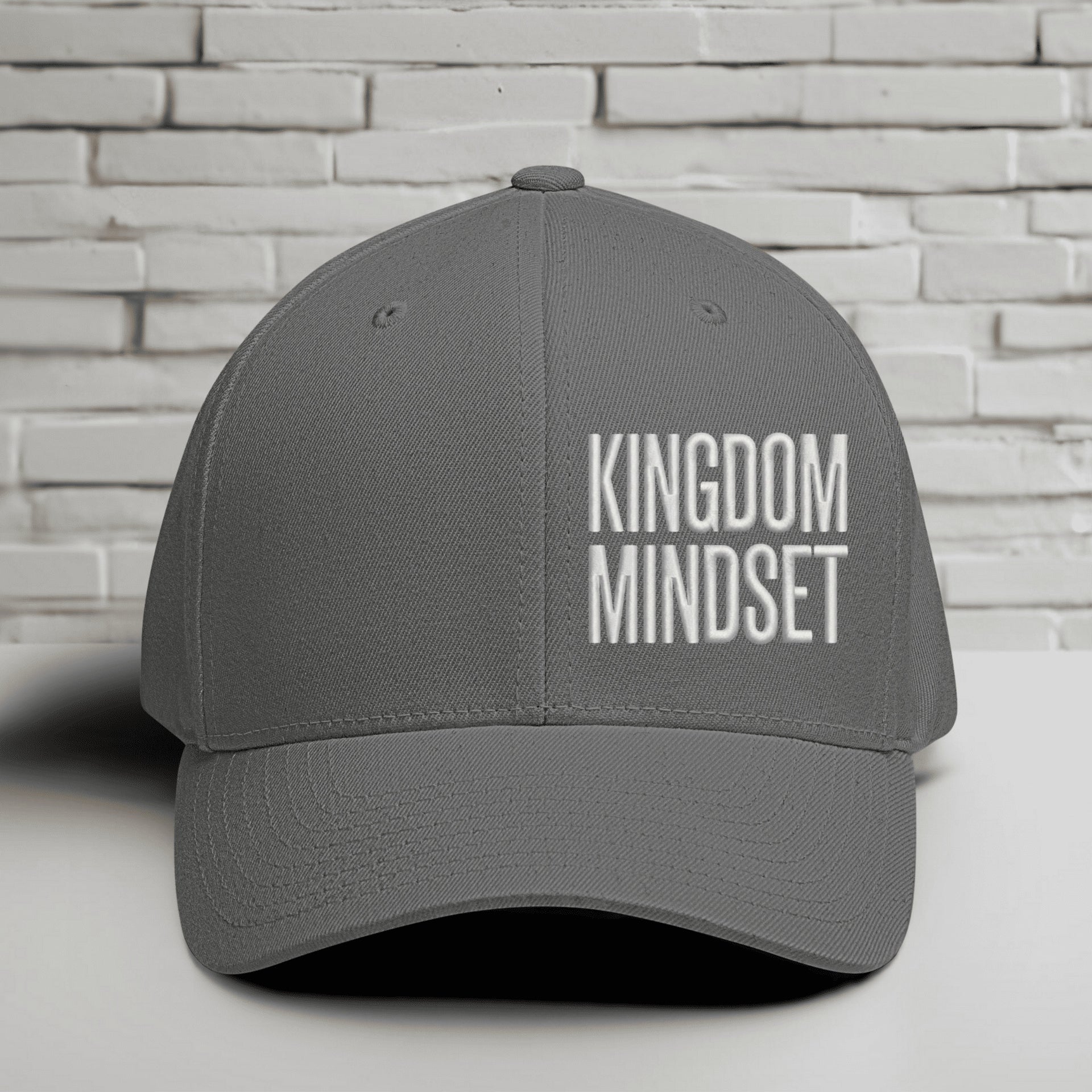Flexfit Kingdom Mindset hat in grey with white embroidery against a brick background.
