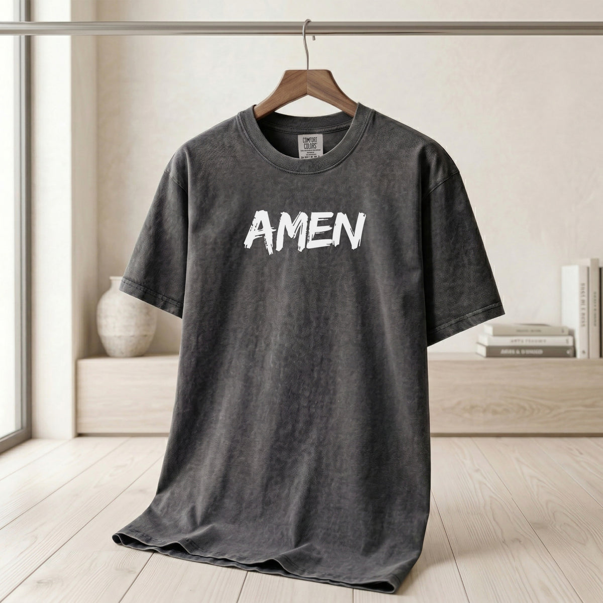 Amen comfort colors t-shirt displayed on a hanger in a bright room, featuring the word 'AMEN' prominently.