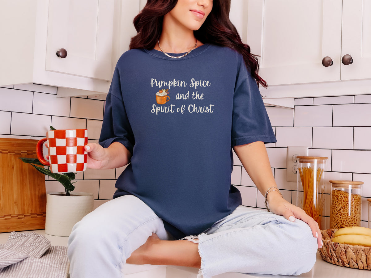 Woman wearing a navy Pumpkin Spice Christian t-shirt, holding a checked mug in a cozy kitchen.