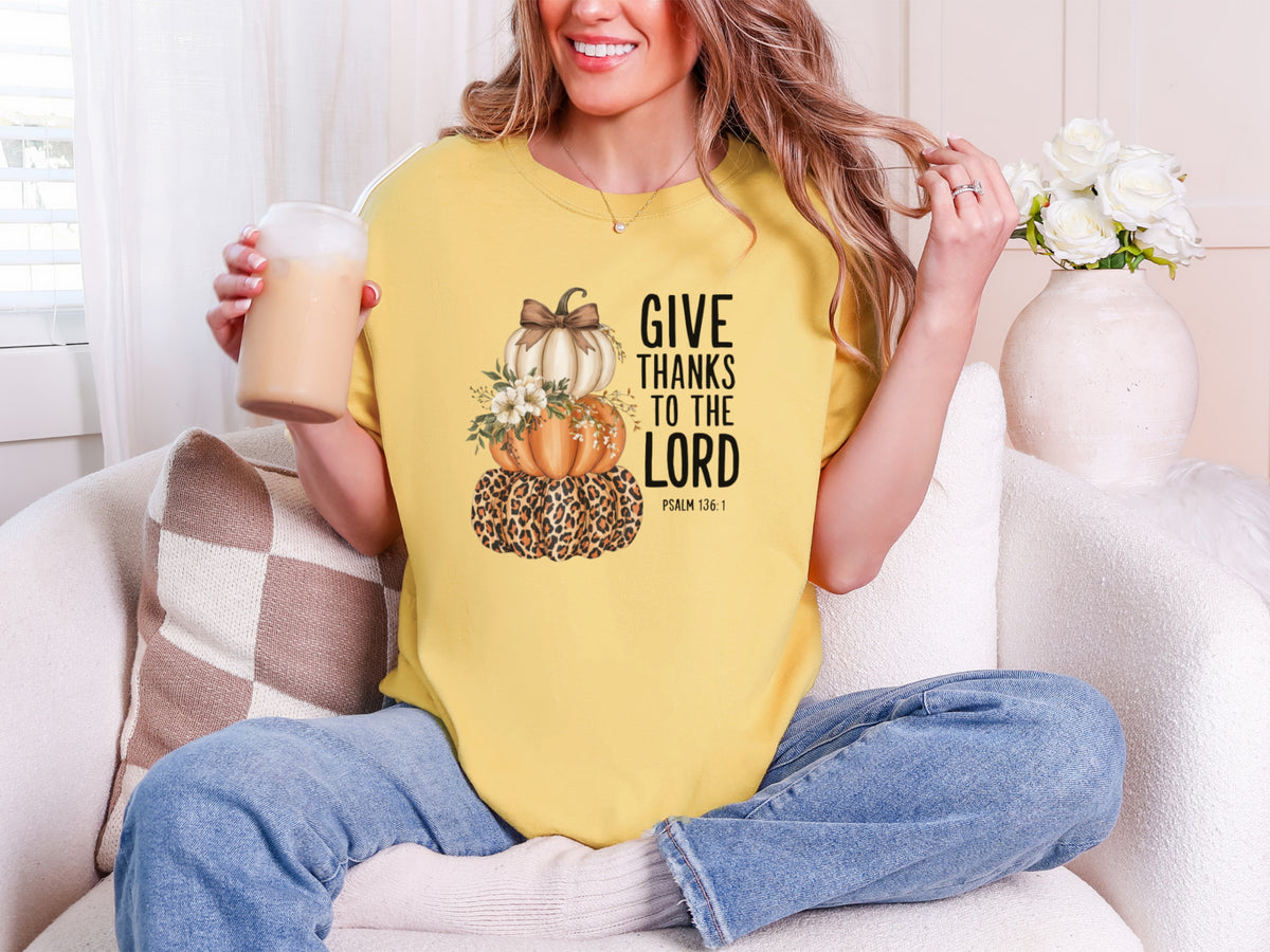 Woman wearing a mustard Give Thanks to the Lord t-shirt with pumpkin design while enjoying a drink.