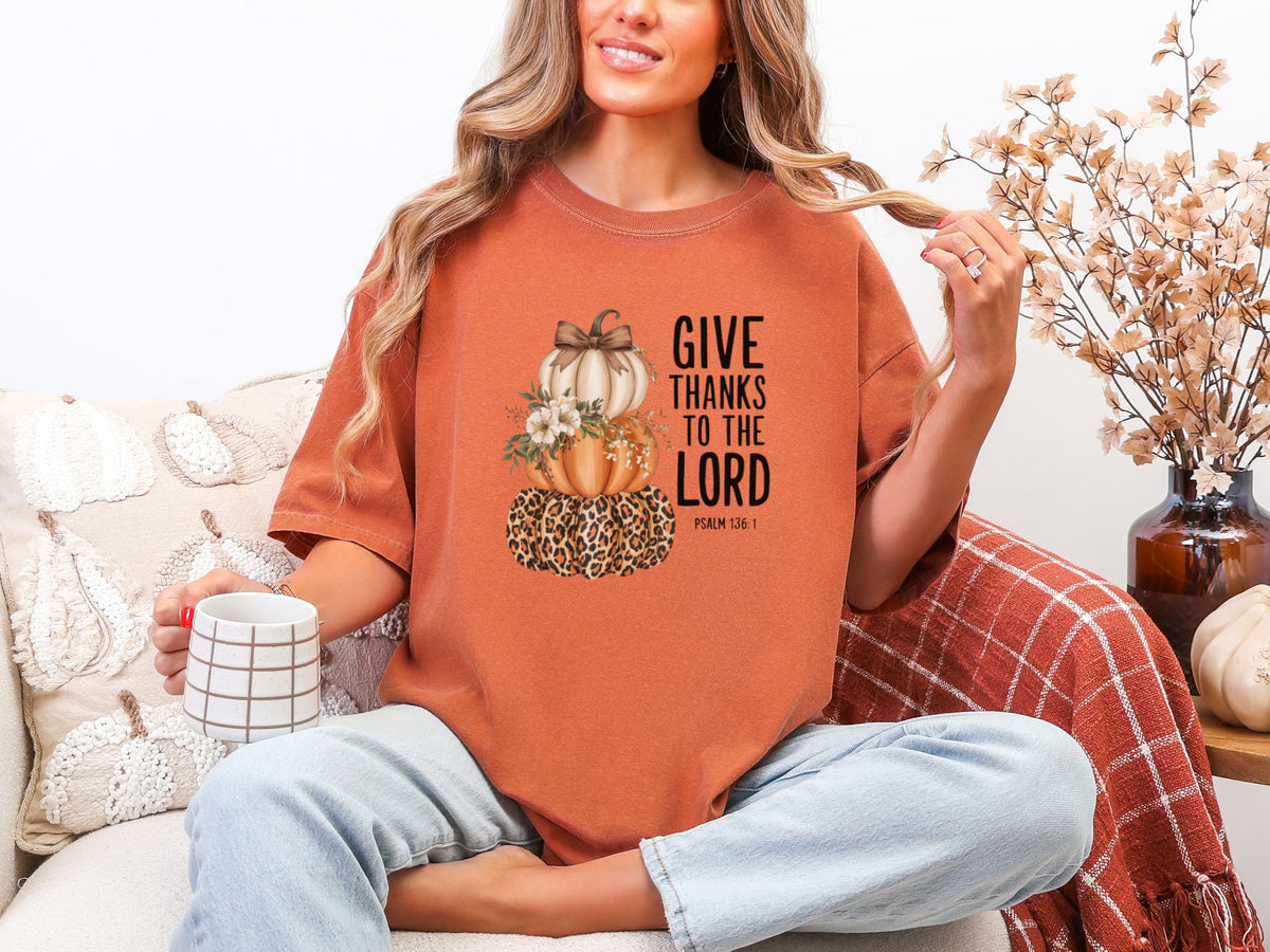 Woman wearing Give Thanks to the Lord T-Shirt in Yam color, featuring pumpkin graphic, sipping coffee.