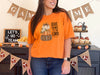 Woman wearing a burnt orange Give Thanks to the Lord t-shirt with pumpkin design at a festive gathering.