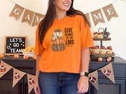 Woman wearing a burnt orange Give Thanks to the Lord t-shirt with pumpkin design at a festive gathering.