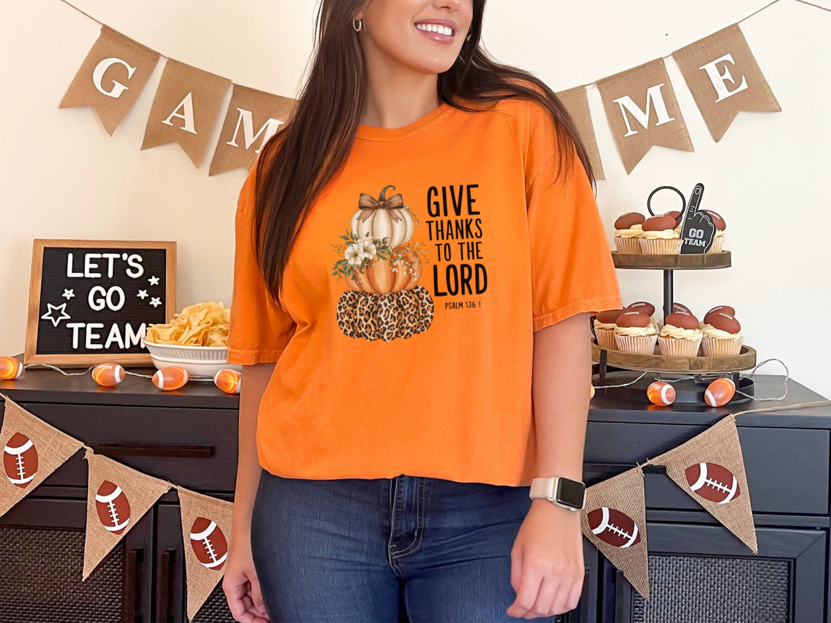 Woman wearing a burnt orange Give Thanks to the Lord t-shirt with pumpkin design at a festive gathering.