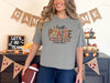 Woman wearing grey Christian graphic tee praise, featuring 'I Will Praise Him in Every Season' surrounded by autumn decor.
